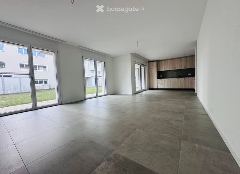 Empty room with large windows, sliding glass doors, tiled floor, wooden cabinets, and a grassy area outside.
