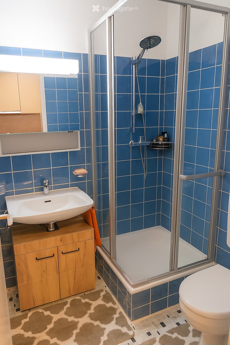 Bathroom with blue tiles, white sink, shower, toilet, wooden cabinet, mirror, and towel
