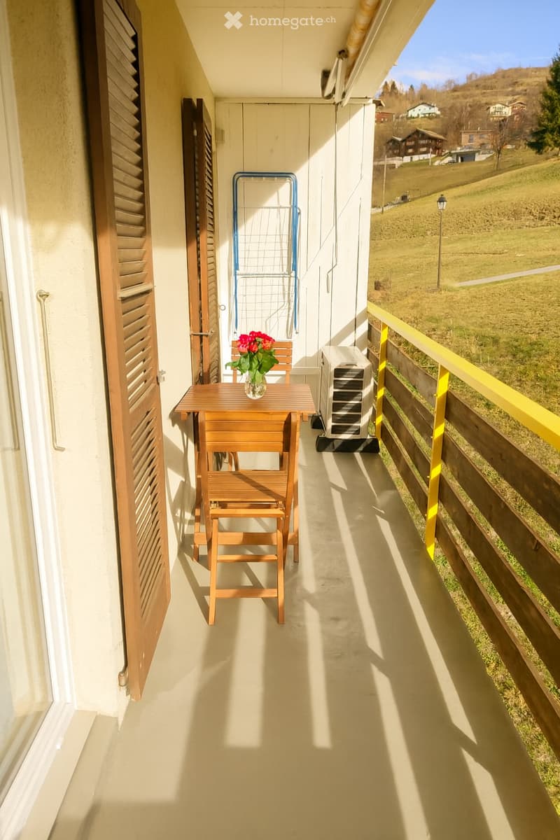 Balcony with table and chairs, flowers, air conditioner, wooden railings, view of the mountains