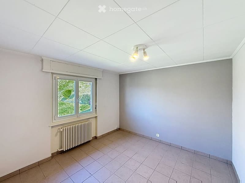 Empty room with white walls, tiled floor, white ceiling, window with white frame, radiator, ceiling lights