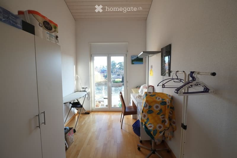 A room with a desk, chair, ironing board, storage boxes, and a coat rack.