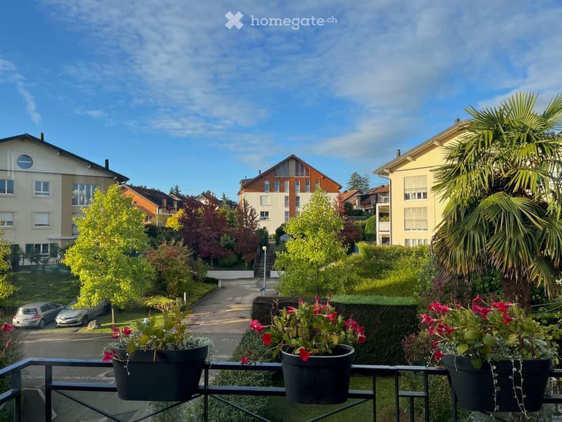 Balcony with view of the street, three buildings, trees, and plants