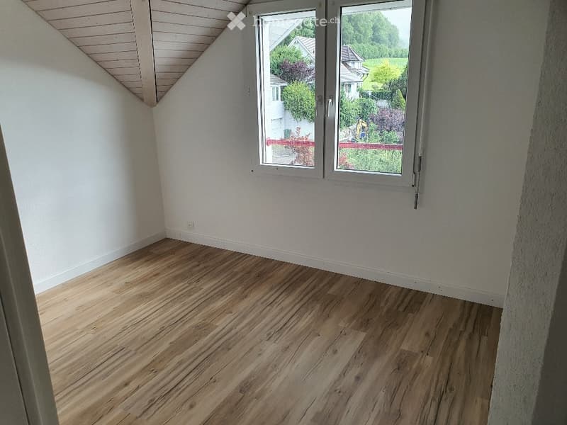 Unfurnished Room. Empty room with wooden floor and white walls. There is a window with a view of a house and garden outside.