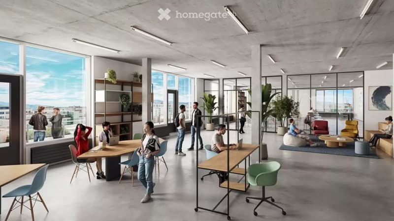 Open office space with desks, chairs, and people working. Large windows provide natural light.