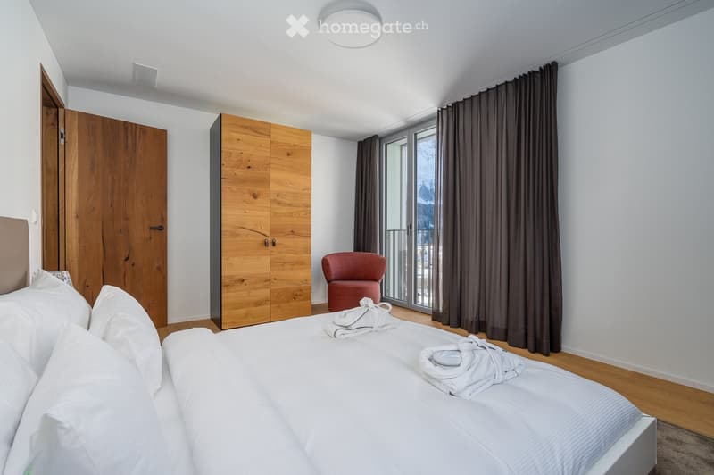 wooden cabinet, white bed, two pillows, a chair, a lamp, windows, curtains