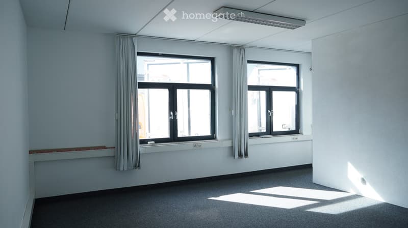 Completely empty room with white walls, gray floor, and two large windows with curtains.