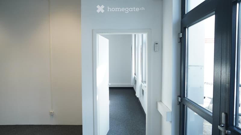 Empty corridor with white walls, gray flooring, and an open door leading to another room.