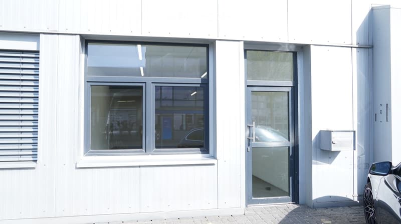 White building with glass windows and a glass door. A car is parked in front.