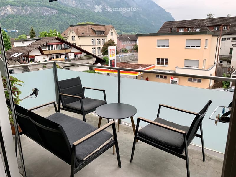 Outdoor balcony with a view of the mountains, featuring three chairs and a small table.