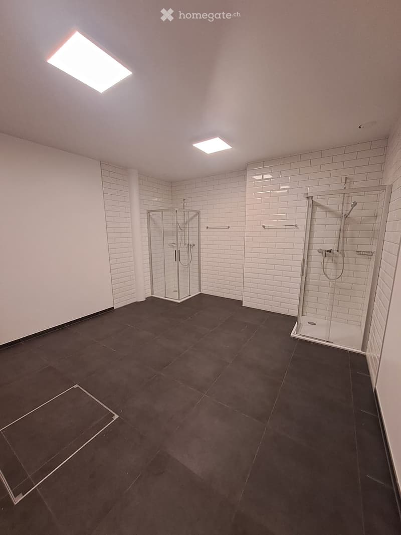 Modern bathroom with dark tiled floor, white brick walls, glass shower stall, and built-in shower area with multiple shower heads.
