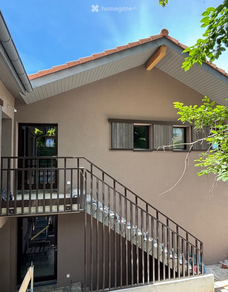 Two-story house with beige stucco walls, red-tiled roof, and multiple windows. A metal staircase leads to an upper-level balcony with a railing.