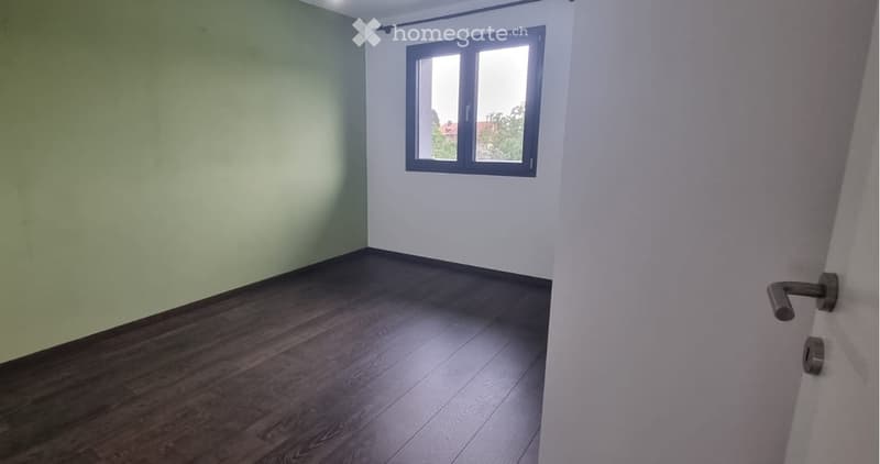 Empty room with wooden flooring, white walls, and a window with a view of trees.