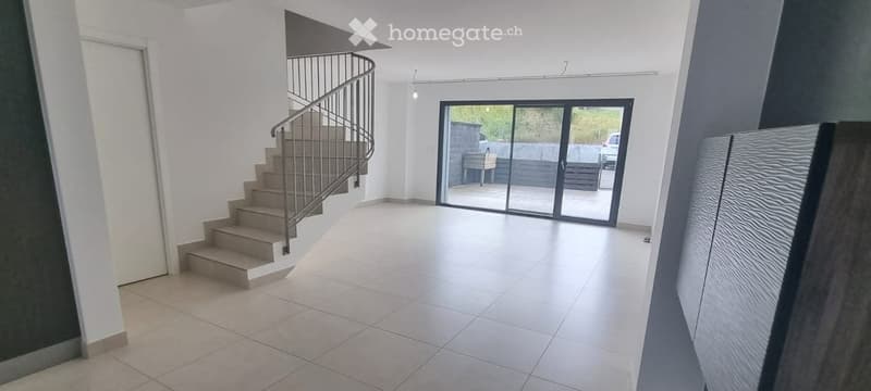 Bright, modern hallway with tiled flooring, a curved staircase with metal railing, and large glass sliding doors leading to an outdoor area.
