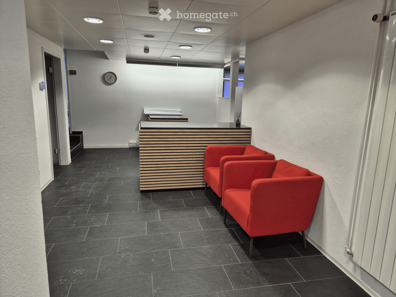 Modern reception area with dark tiled flooring, white walls, a reception desk, and red chairs.