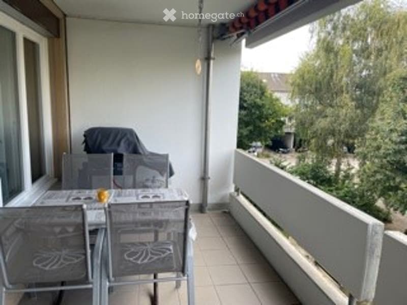 Balcony / Terrace. Balcony with tiled floor, white railing, outdoor table and chairs, umbrella, and view of greenery.