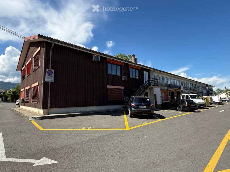 Building. Two-story building with brown siding and multiple windows, with a parking lot in front containing several cars.