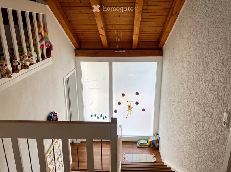 Corridor / Hallway. Staircase with wooden railings, plush toys on a shelf, books stacked on the floor, and a frosted glass door with festive decorations.