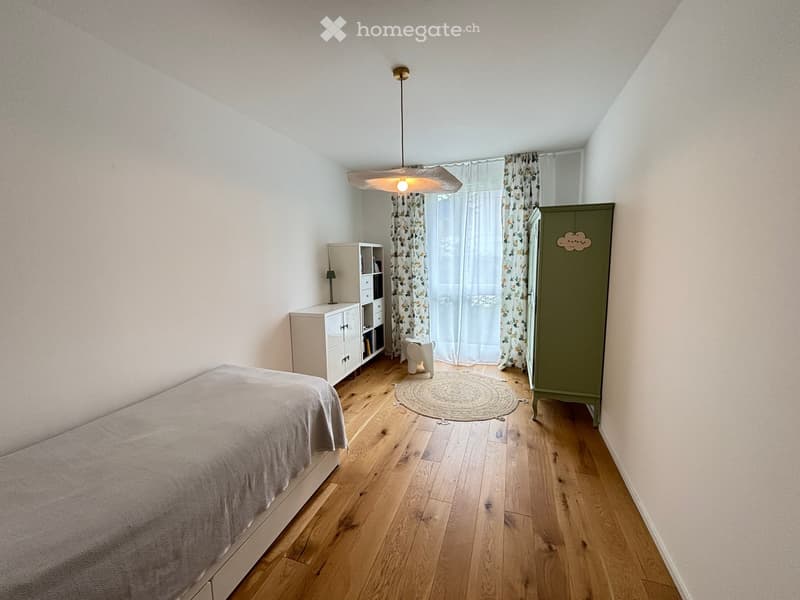 Bedroom. Cozy bedroom with wooden flooring, a bed with a grey duvet, a green wardrobe, a white nightstand with a lamp, and a round woven rug.
