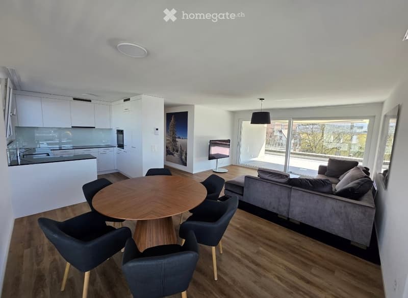 Furnished Room. Modern open-plan living and dining area with a grey sofa, wooden coffee table, dining table with chairs, and a sleek kitchen area with white cabinets and a sink.