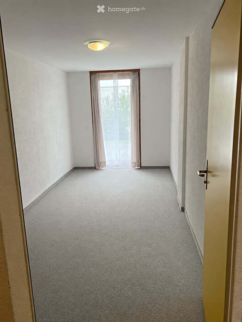 Unfurnished Room. Empty hallway with carpeted floor, white walls, a single ceiling light, and a window with curtains at the end.