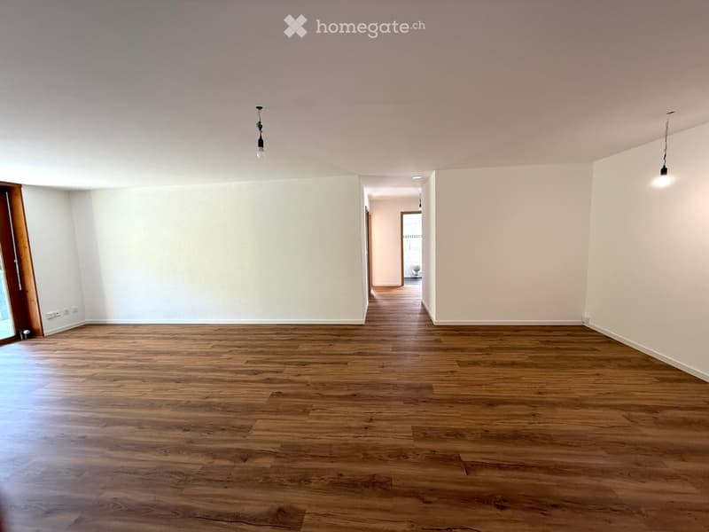 An empty room with wooden floors, white walls, and three light fixtures hanging from the ceiling.