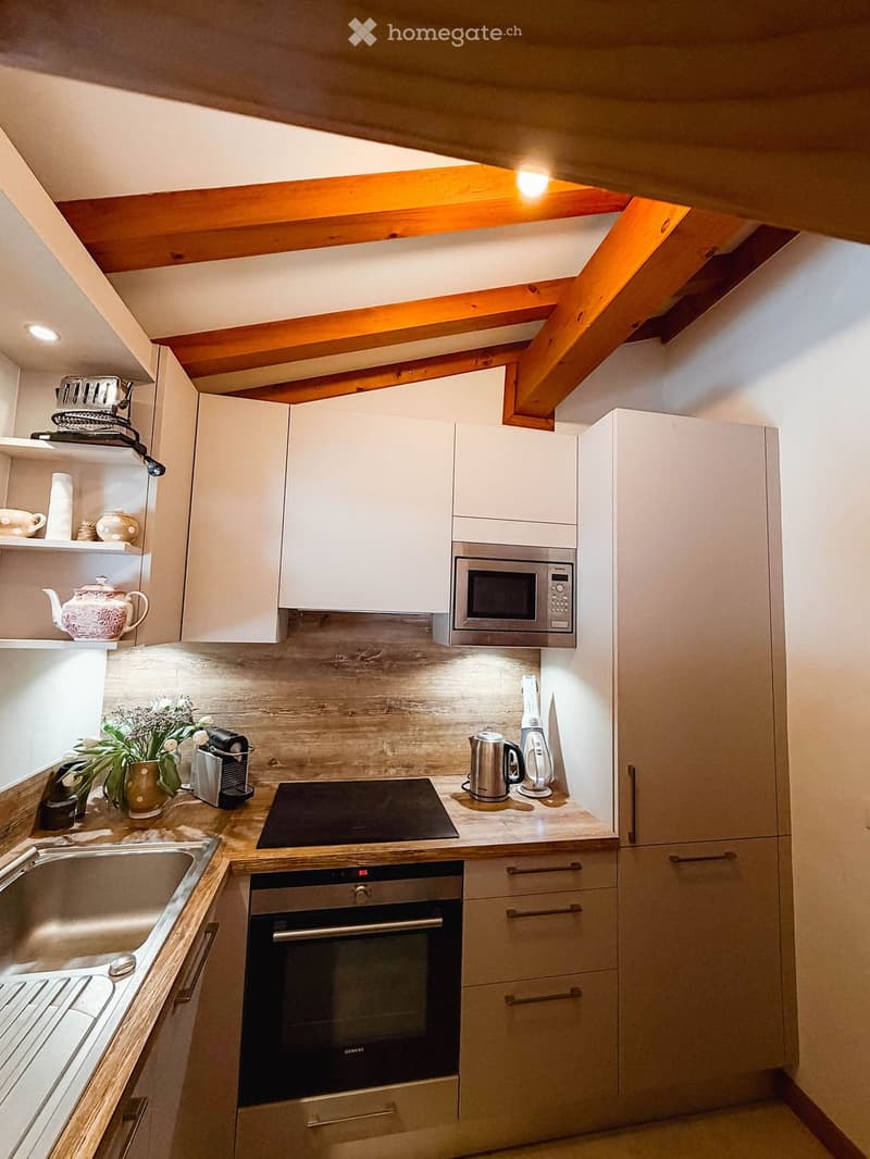 Modern kitchen with white cabinets, stainless steel appliances, wooden countertops, and exposed wooden beams on the ceiling.