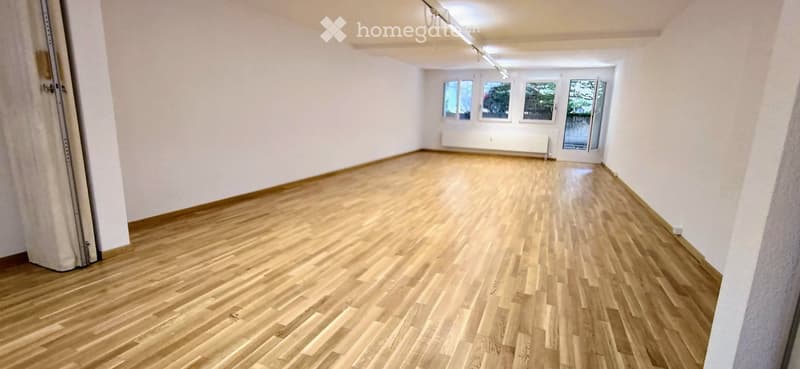 Empty room with wooden flooring and white walls, featuring large windows and a radiator.