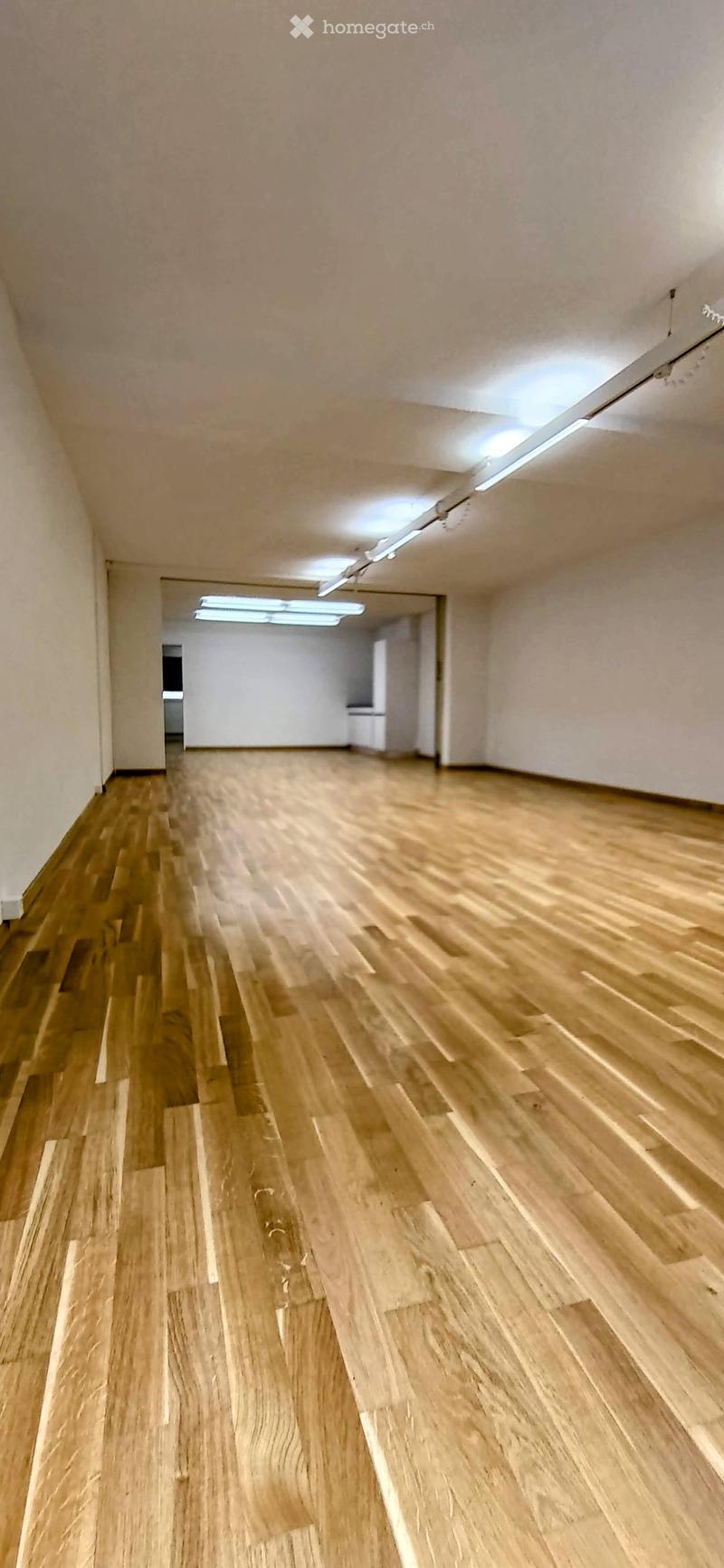 Empty room with wooden flooring and white walls, featuring a doorway leading to another room.