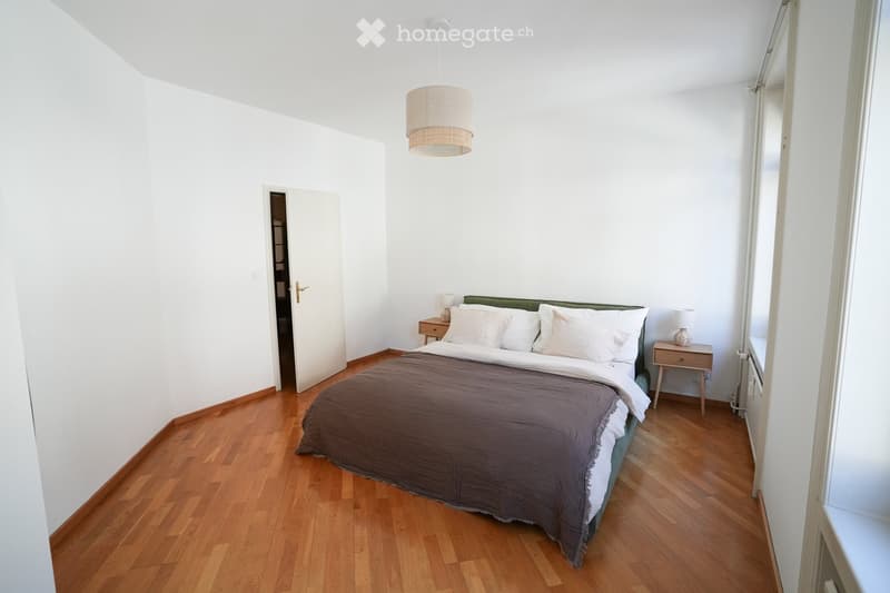 Bright bedroom with wooden flooring, a double bed with a dark brown duvet, two nightstands with lamps, and a pendant light hanging from the ceiling.
