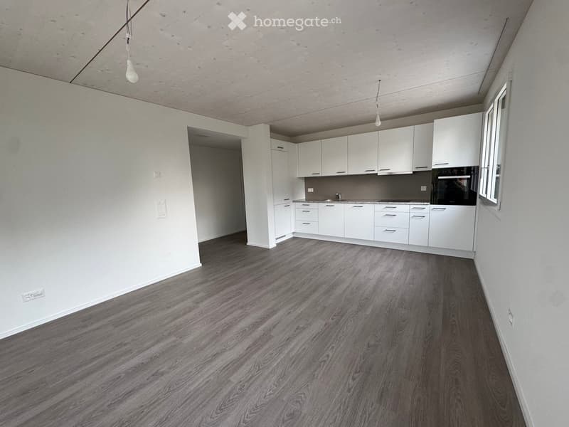 Empty kitchen with white cabinets, dark wooden flooring, and a window on the right side.