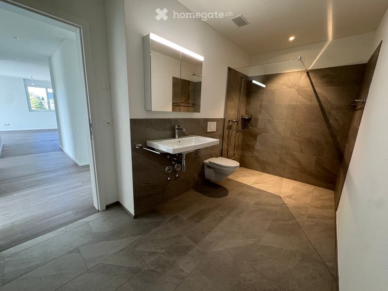 Modern bathroom with a white sink, toilet, large mirror, and glass-enclosed shower area. The space features beige tiles and a sleek design.