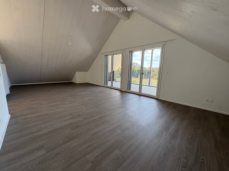 Empty attic room with wooden flooring, large skylight windows, and exposed wooden beams on the ceiling.