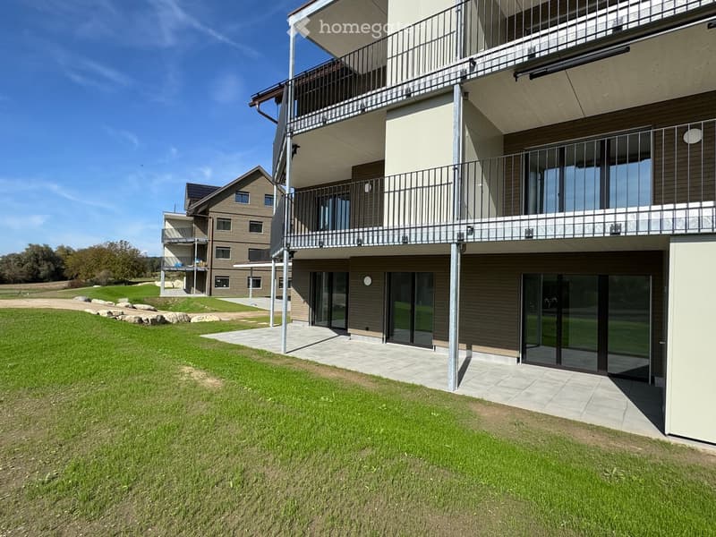 Modern two-story building with balconies, large windows, and a well-maintained lawn in front.