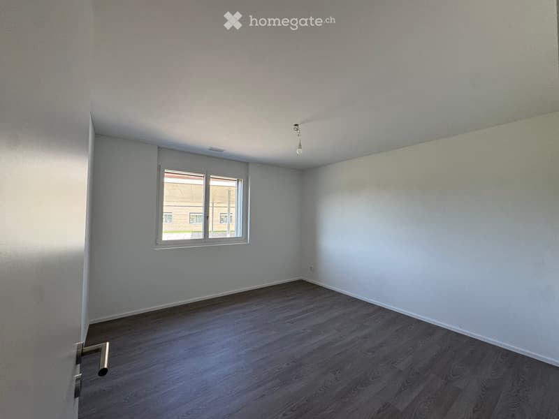Empty room with light grey walls, wooden flooring, and a single window with white frame. No furniture or equipment present.