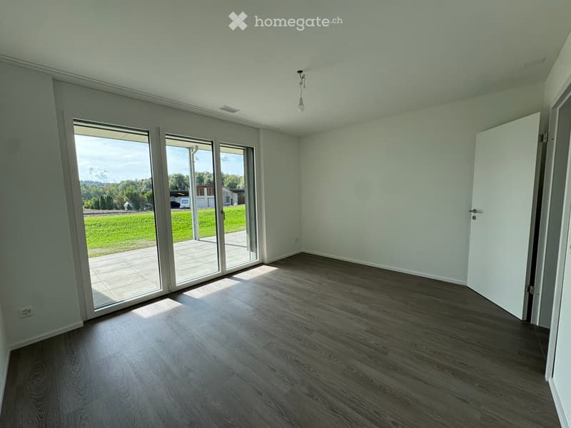 Empty room with light-colored walls, wooden flooring, and large sliding glass doors leading to a patio and outdoor area.