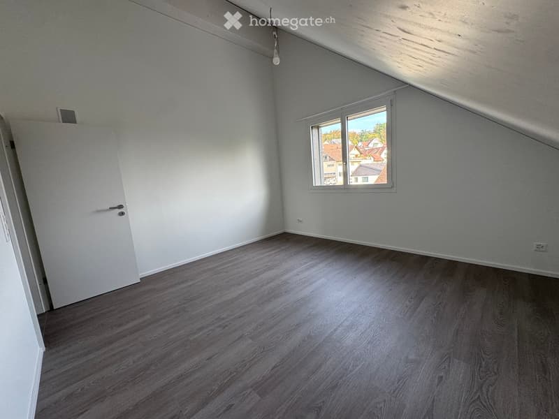 Empty room with light grey walls, dark wooden flooring, and a single window showing a view of neighboring houses.