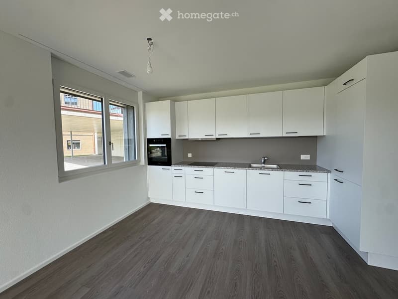 Modern kitchen with white cabinets, dark wooden flooring, and large windows offering a view of the outside.