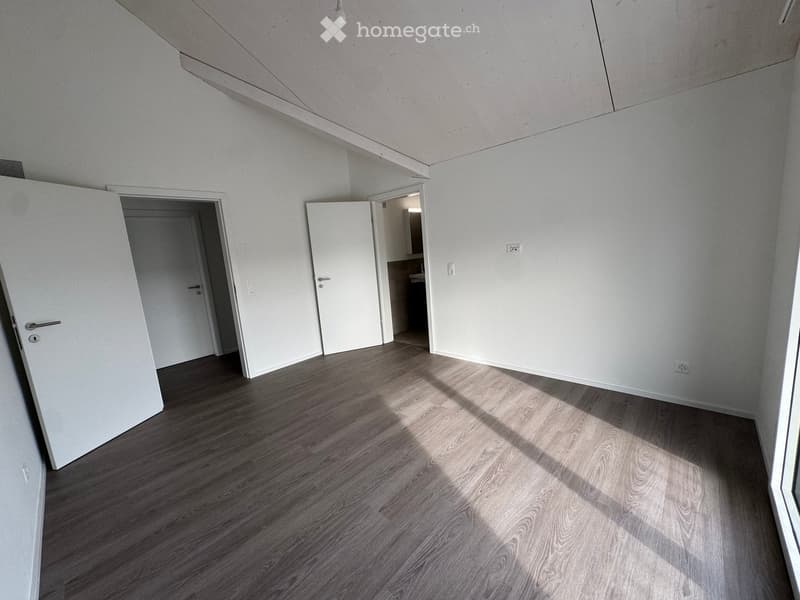 Empty room with light wooden flooring and white walls, featuring two open doors leading to adjacent spaces.