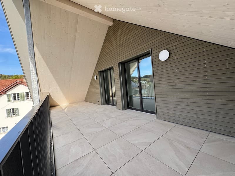Modern balcony with tiled floor, wooden paneling, large glass sliding doors, and a metal railing.