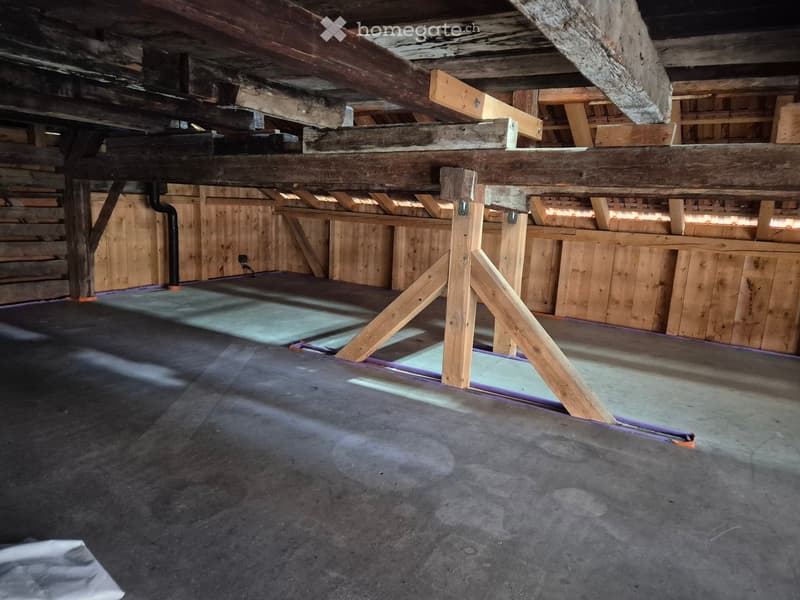 Empty attic space with exposed wooden beams and concrete floor, featuring wooden crates and storage boxes along the walls.