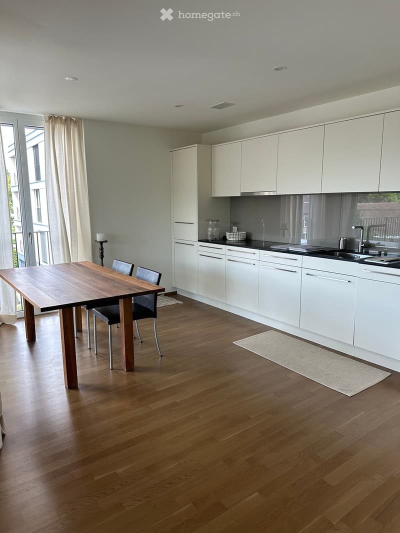 Modern kitchen and dining area with white cabinets, wooden floor, dining table, chairs, and a sink.