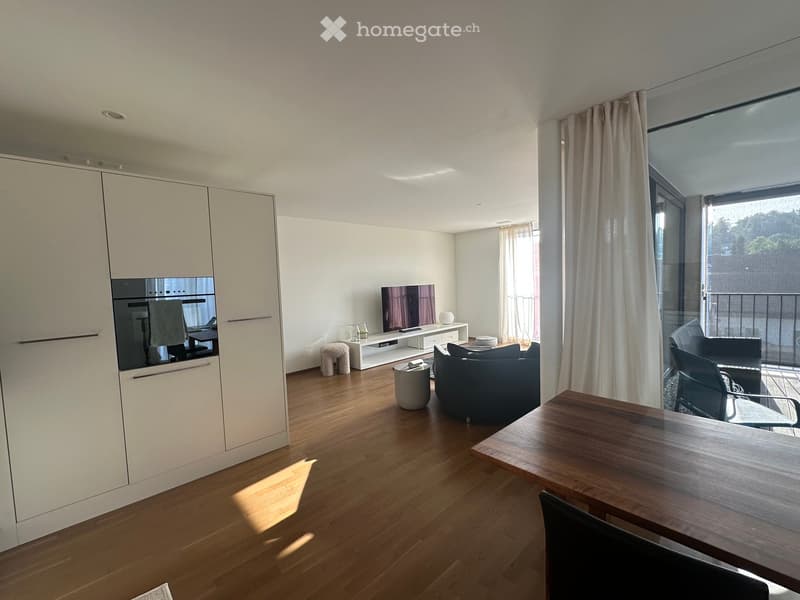 Modern living room with wooden flooring, large windows, balcony access, sofa, coffee table, TV, and chairs.