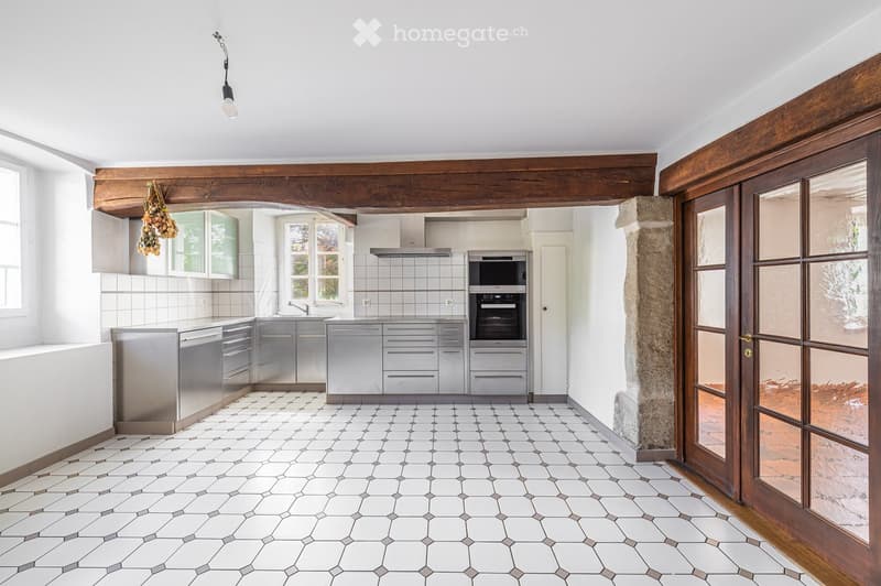 Modern kitchen with stainless steel appliances, white tiled walls, and hexagonal tile flooring. Features include a built-in oven, microwave, and a hanging light fixture.