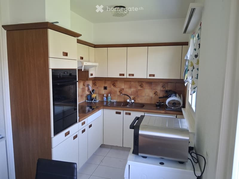 A compact kitchen with white cabinets, a dark oven, a sink, a toaster, and a dish rack. The backsplash features a floral tile design.