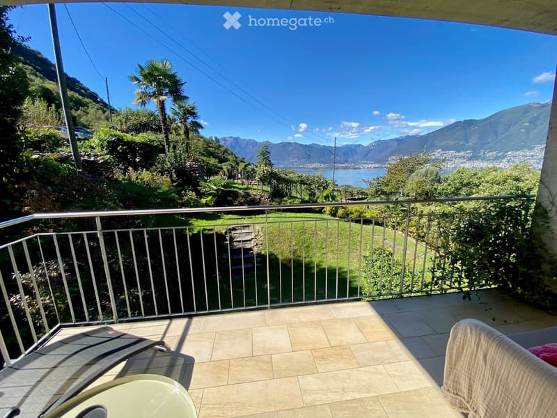 Balcony with a scenic mountain and lake view, featuring a tiled floor, metal railing, and outdoor furniture including a chair and table.