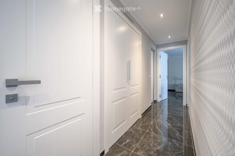 Corridor / Hallway. Empty corridor with white doors, marble flooring, and a chevron pattern on the wall.