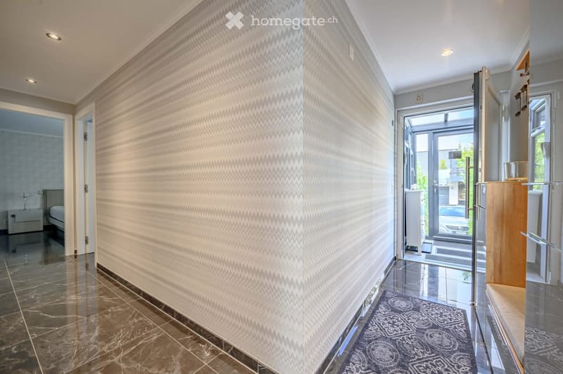 Corridor / Hallway. A hallway with a zigzag patterned wall, marble flooring, and a rug. There is a bed and nightstand in the background.