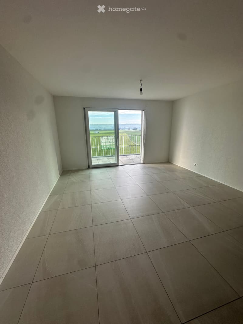 Empty room with tiled floor, white walls, and a sliding glass door leading to a balcony with a view of the countryside.