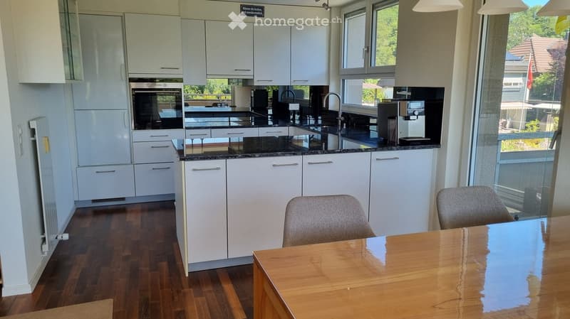 Modern kitchen with white cabinets, black countertops, stainless steel appliances, and a wooden dining table with chairs.