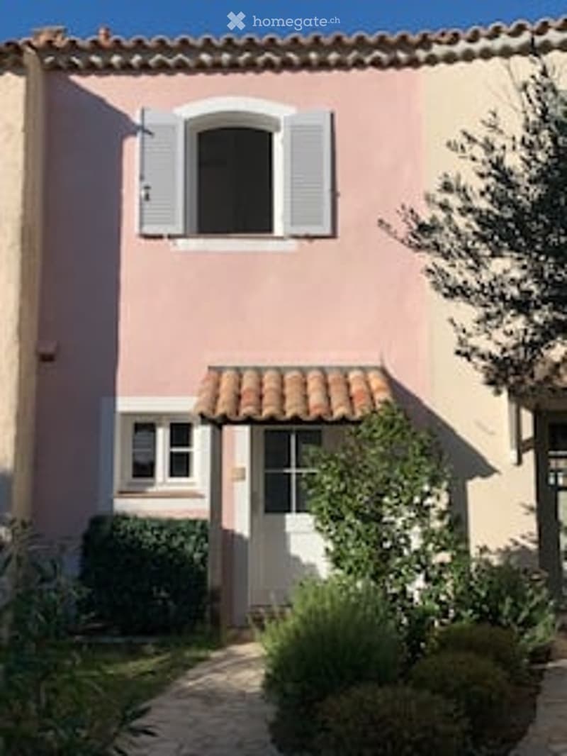 Two-story house with pink and beige exterior, white shutters, tiled roof, small garden, and pathway.